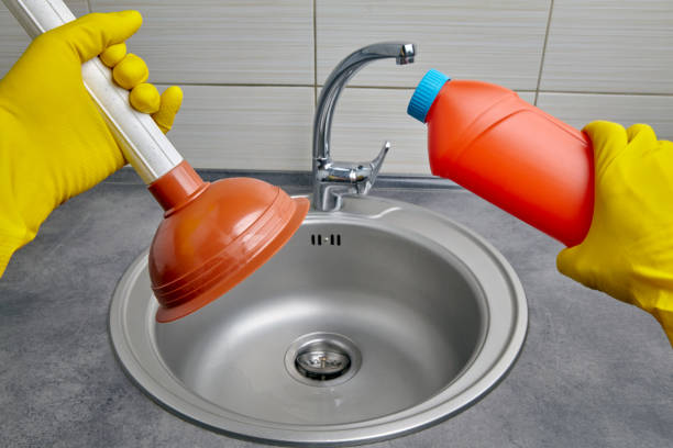 hands in yellow rubber gloves hold a plunger and pipe cleaner - sink drain plumber domestic kitchen imagens e fotografias de stock