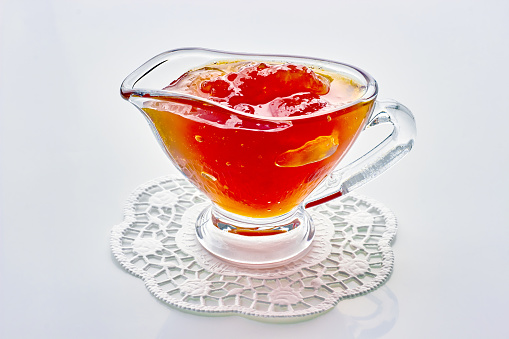 Homemade sweet fruit jam in a glass gravy boat on an openwork napkin isolated on a white background
