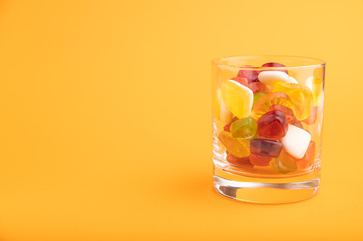 Various fruit jelly candies in drinking glass on orange pastel background. side view, copy space.