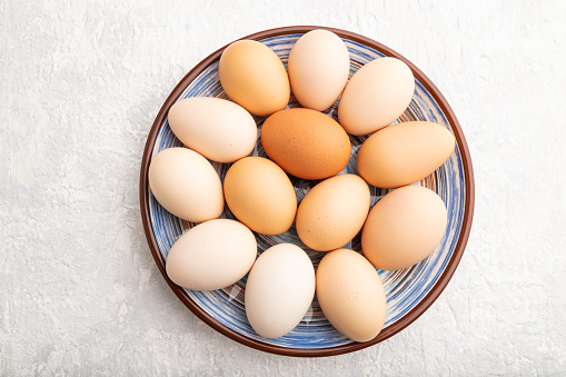 Pile of colored chicken eggs on plate on a gray concrete background. top view, flat lay, close up.