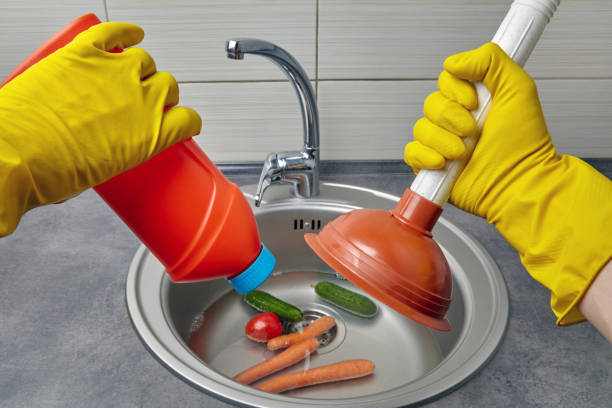 hands in yellow rubber gloves hold a plunger and pipe cleaner - sink drain plumber domestic kitchen imagens e fotografias de stock