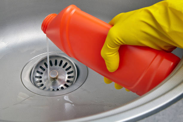 hands in yellow rubber gloves pour sewer pipe cleaner down the kitchen sink drain - sink drain plumber domestic kitchen imagens e fotografias de stock