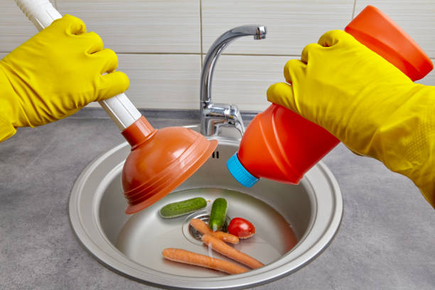 hands in yellow rubber gloves hold a plunger and a pipe cleaner - sink drain plumber domestic kitchen imagens e fotografias de stock