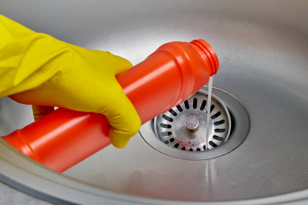 Person's hand in a yellow rubber glove pours pipe cleaner down the drain of a metal kitchen sink Person's hand in a yellow rubber glove pours pipe cleaner down the drain of a metal kitchen sink. Prevention and cleaning of sewer blockages cleaner stock pictures, royalty-free photos & images