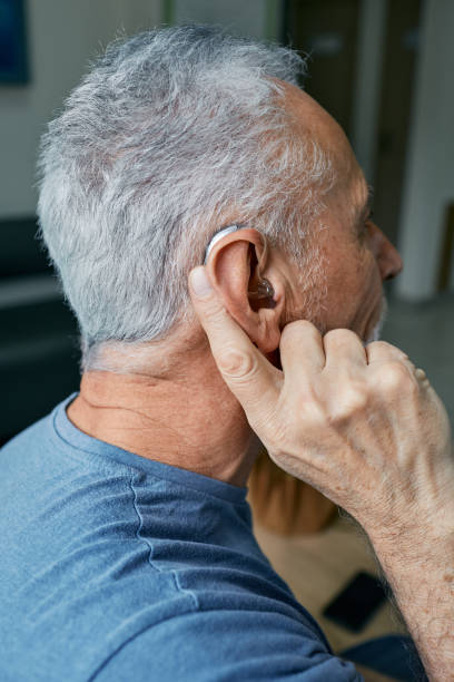 istock Senior man tunes his hearing aid behind the ear by pressing his finger on setting button. Modern hearing aid, hearing solutions 1402639196