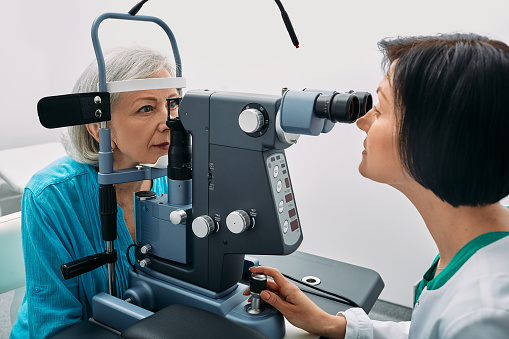 Female optometrist doing sight test to senior woman at modern ophthalmology clinic. Eye exam and vision diagnostic