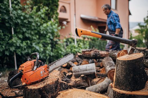 Chainsaw and ax on piles of cut firewood