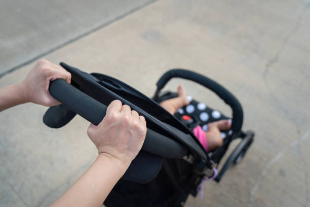Action of a mother hand is holding and pushing on baby stroller or cart for walking on the road. Happiness parenthood concept scene.