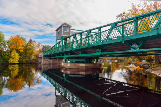 Road bridge over a river with wooded banks in autumn Swing bridge across a river on a partly cloudy autumn day. Reflection in water. Huntsville, ON, Canada. huntsville ontario stock pictures, royalty-free photos & images