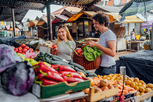 Young cheerful couple buying vegetable at public market