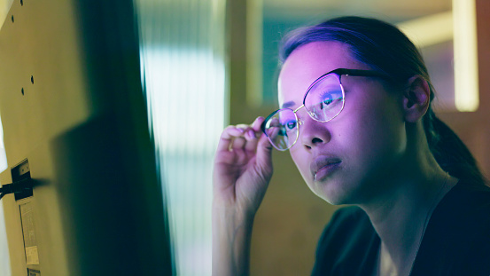 Close-up image of an Asian woman studying information on a computer screen.
She’s in a small office with the screen lighting up her face.