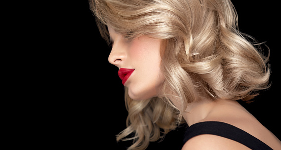 Young woman is demonstrating perfect wisps on the middle length hairstyle dyed in shades of blonde and silver color. Bright makeup with long, blacked eyelashes and vivid red lipstick.  Hairstyling, dye of hair, cosmetics and makeup.