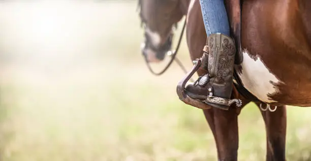 Photo of Detail of a ornamented cowboy boots in a stirrup while sitting on a horse.