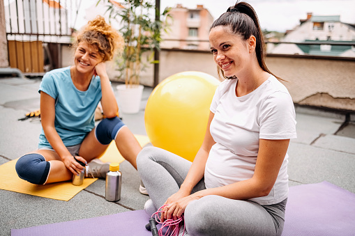 Two young women are sitting on exercise mats and looking at the camera