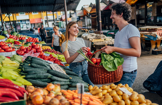 Young cheerful couple buying vegetable at public market