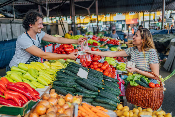 Paying with a smile on her face Seller man taking cash from cheerful woman customer at the public market farmers market healthy lifestyle choice people stock pictures, royalty-free photos & images