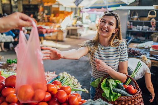 Young cheerful woman buying fresh vegetables at market