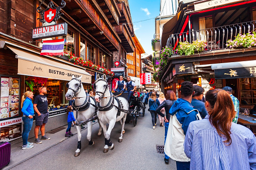 ZERMATT, SWITZERLAND - JULY 15, 2019: Horse coach and traditional local houses in the centre of Zermatt town in the Valais canton of Switzerland