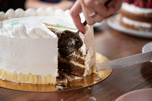Closeup view of a woman cutting and serving delicious vegan birthday cake with cream frosting.