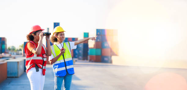 istock binoculars and walkie talkie. Black female dock worker control loading containers box from cargo at warehouse container yard. Marine and carrier insurance concept. 1402660107