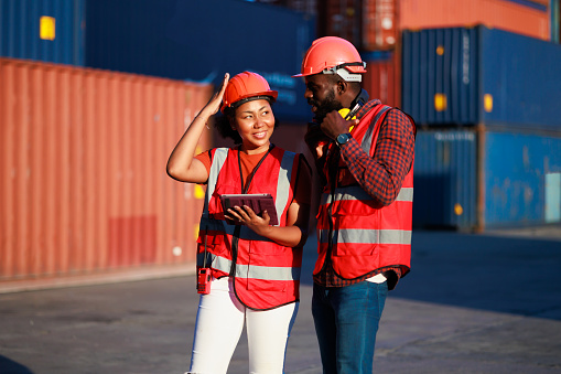 Portriat handsome male African American Industrial and female cock warehouse specialist. Black man worker wearing yellow protective hard hat helmet working at container yard.