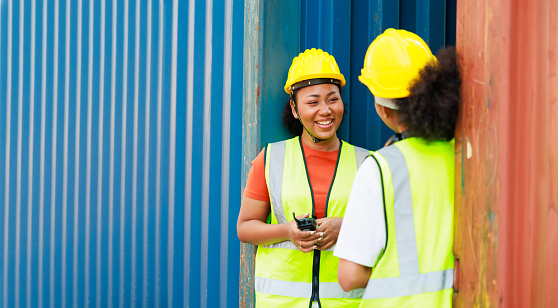 Two friends Black female dock worker relax talking in break time at warehouse container yard. Marine and carrier insurance concept. logistic shipping yard