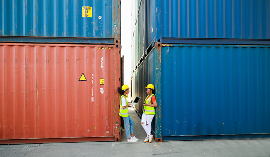 Two friends Black female dock worker relax talking in break time at warehouse container yard. Marine and carrier insurance concept. logistic shipping yard