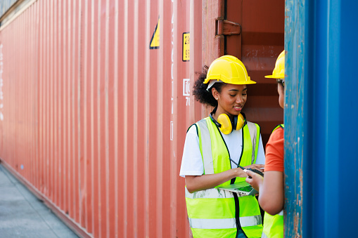 Two friends Black female dock worker relax talking in break time at warehouse container yard. Marine and carrier insurance concept. logistic shipping yard