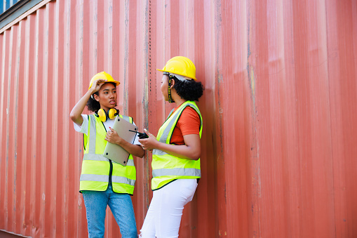 Two friends Black female dock worker relax talking in break time at warehouse container yard. Marine and carrier insurance concept. logistic shipping yard