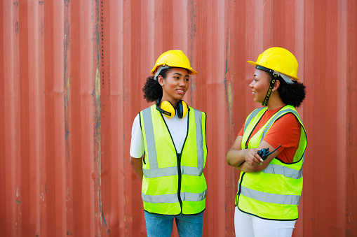 Two friends Black female dock worker relax talking in break time at warehouse container yard. Marine and carrier insurance concept. logistic shipping yard