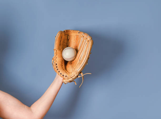 istock Baseball leather glove with white ball on woman's hand on blue background. 1402660708