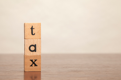 tax. tax character. Written in lowercase letters on a wooden block. Written on three blocks stacked on a wooden table. Gray background. Copy space on the right.