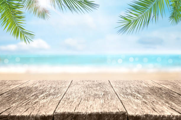 Wood table over sea and beach background in summer day. Empty wood table over blue sea, beach and palm leaves background in summer day. Background with copy space for product display. beach bar stock pictures, royalty-free photos & images