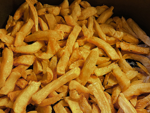 Stock photo showing the inside of an air fryer with a pile of golden brown, freshly cooked French fries / chunky chips. Healthy cooking concept.