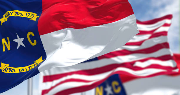 The North Carolina state flag waving along with the national flag of the United States of America The North Carolina state flag waving along with the national flag of the United States of America. In the background there is a clear sky. North Carolina is a state in the Southeastern region of the United States north carolina us state stock pictures, royalty-free photos & images