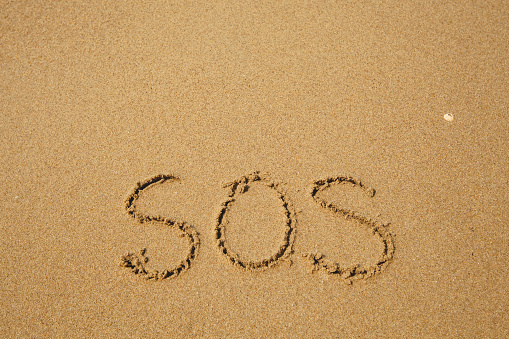 SOS - handwritten on the soft beach sand.