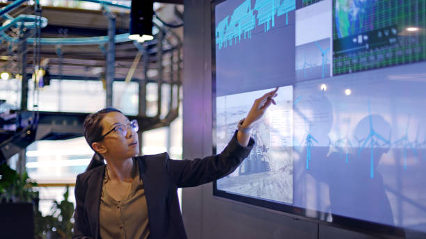 Energy lecture screen Stock photograph of a young Asian woman conducting a seminar / lecture with the aid of a large screen. The screen is displaying data & designs concerning low carbon electricity production with solar panels & wind turbines. These are juxtaposed with an image of conventional fossil fuel oil production. power equipment stock pictures, royalty-free photos & images