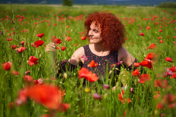 Curly hair redhead woman in floral dress in a poppy field
