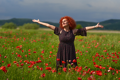 Curly hair redhead woman in floral dress in a poppy field