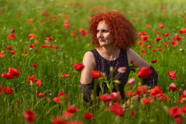 Curly hair redhead woman in floral dress in a poppy field