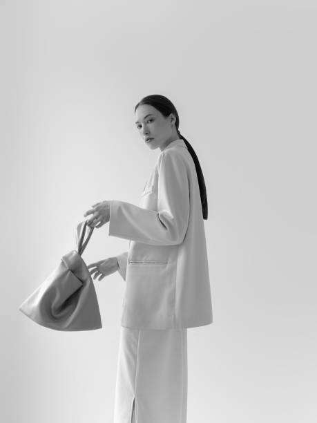 Young beautiful woman wearing Elegant unique luxury clothing collection Mixed Asian and Caucasian girl Fashion model in light blazer skirt holding designer bag Korean style Studio shot with natural lighting High Quality Shopping advertising concept Looking at camera Perfect for you shop boutique designer studio advertising campaign and websites Calm natural beauty High quality picture joven hermosa mujer vestida elegante colección de ropa de lujo única mixta asiática y caucásica modelo de moda en falda blazer ligera sosteniendo bolso de diseñador estilo coreano foto de estudio con iluminación natural alta calidad concepto publicit