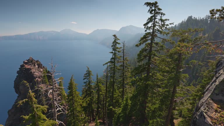 Rocks, trees and blue lake in Crater Lake National Park, Oregon, USA. Gimbal shot on cliff with stones, 4K