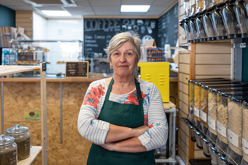 Woman working in a cafe/store that promotes sustainable living in the North East of England. The store has refill stations to reduce plastic and food waste. She is wearing an apron, looking at the camera while smiling.