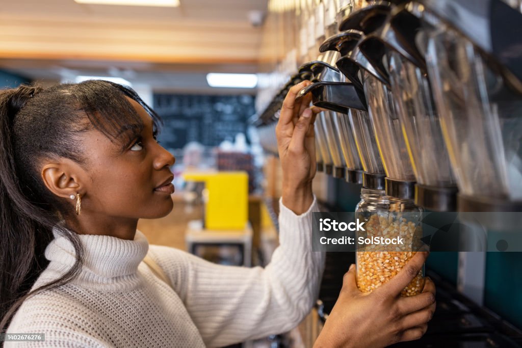 Stocking Up on Corn Kernels Side view of a customer shopping in a store that promotes sustainable living in the North East of England. The store has refill stations to reduce plastic and food waste. She is filling up a glass jar with popcorn kernels. Jar Stock Photo