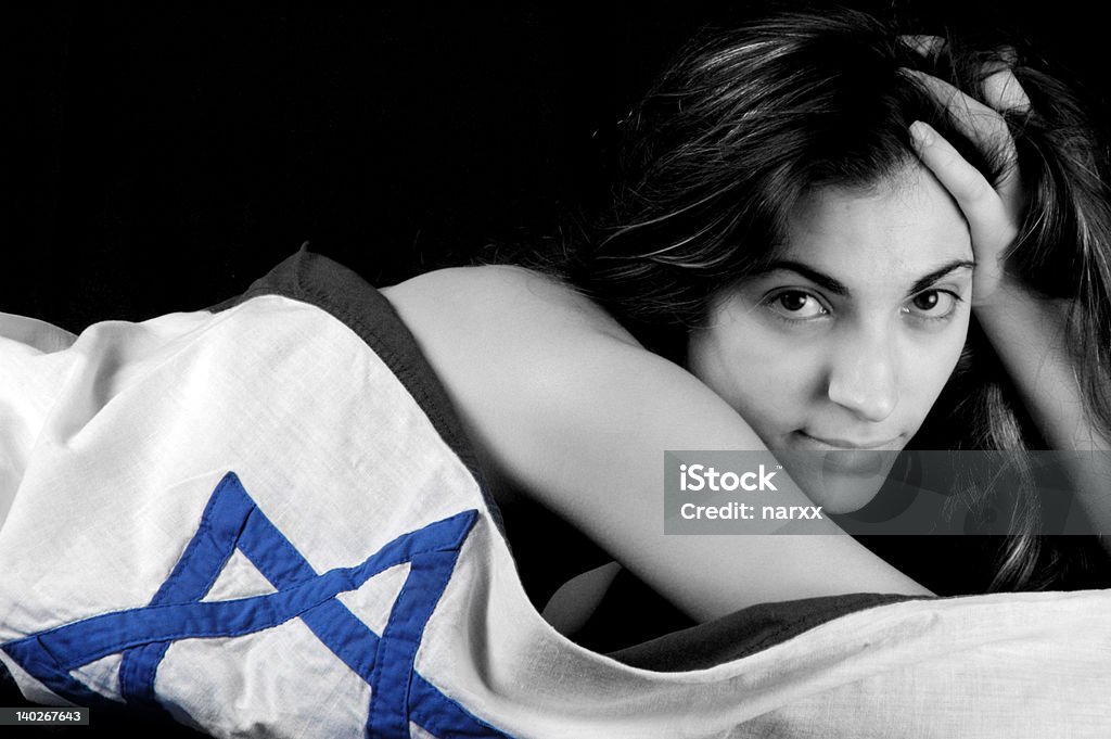 Girl wearing Israel flag #9 A girl lying on the floor, looking towards camera, covered with Israel flag. Black and white. Color, Isolated on black background. Abdomen Stock Photo