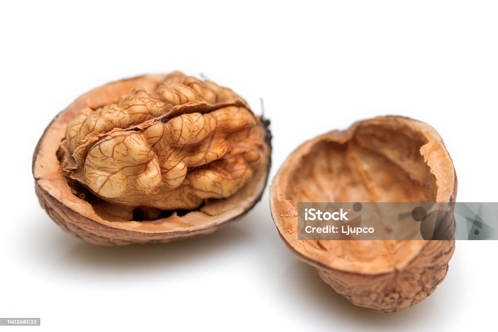 Walnut shell cracked in half to show nut Close-up of a walnut against white background Brown Stock Photo