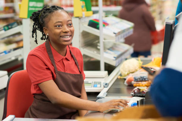 istock Happy young cashier in workwear looking at customer while sitting by workplace 1402680556