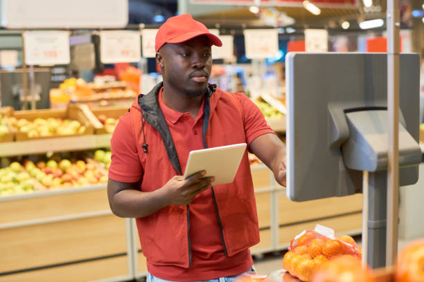 istock Black man in workwear pushing button on screen of electronic scales 1402680618