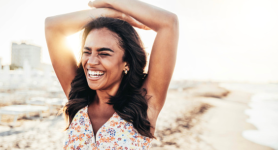 Happy young black woman smiling relaxing on the beach - Cheerful female having fun on summer vacation - Mental health, freedom and happiness lifestyle concept