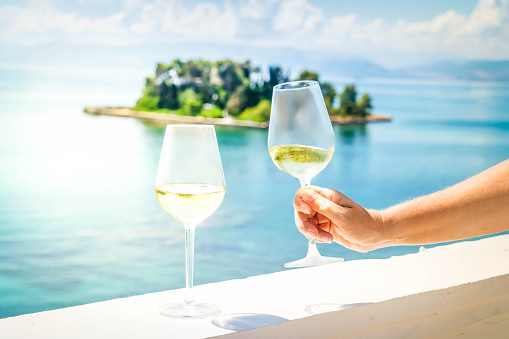 Hand holding one of the glasses of white wine with Corfu seascape in background